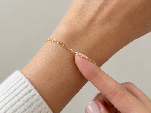 Fingertip under a thin gold permanent bracelet showing a comfortable fit