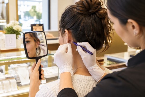 Jewelry store associate marking earlobe placement before ear piercing while customer checks the spot in a mirror